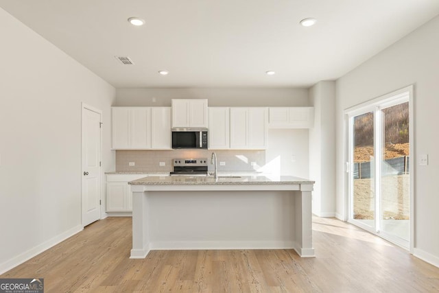 kitchen with appliances with stainless steel finishes, white cabinetry, an island with sink, sink, and backsplash