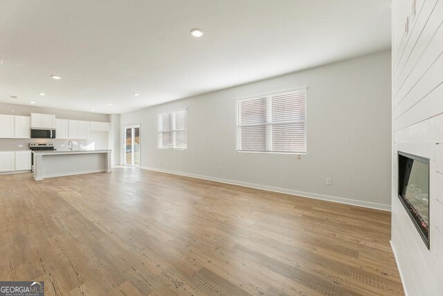 unfurnished living room featuring a fireplace, sink, and light wood-type flooring