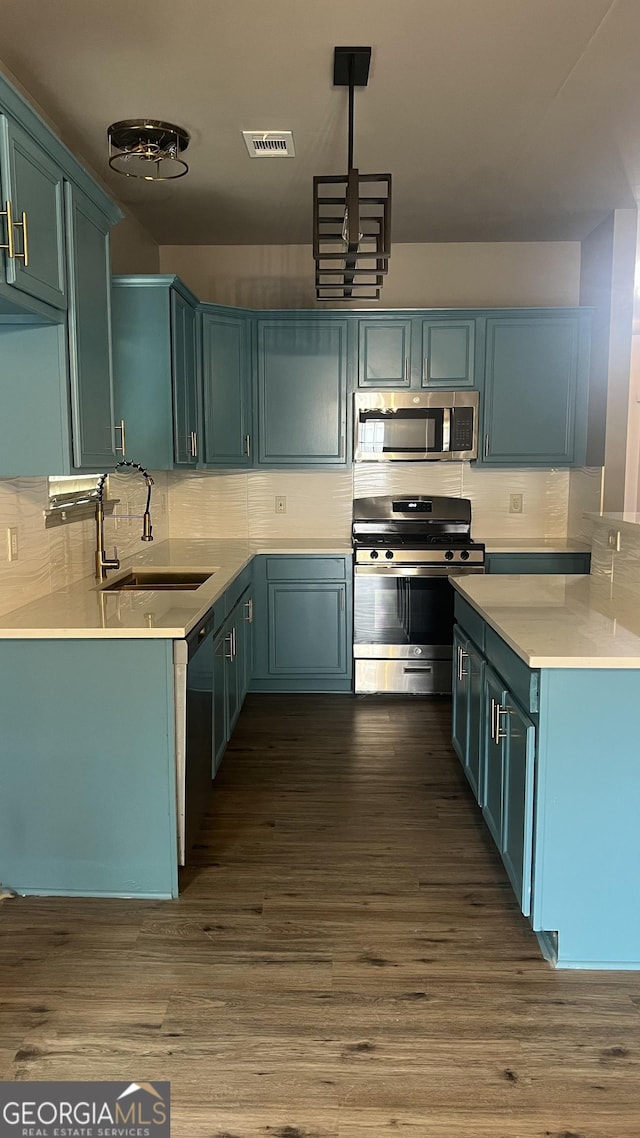 kitchen with sink, dark wood-type flooring, appliances with stainless steel finishes, hanging light fixtures, and decorative backsplash