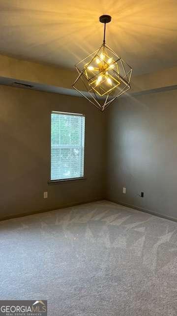 carpeted empty room with an inviting chandelier