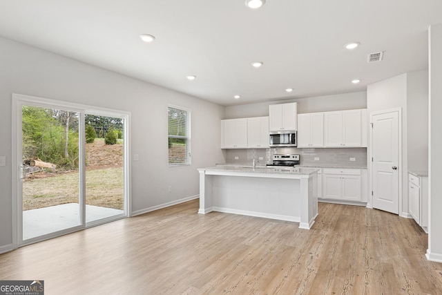 kitchen featuring backsplash, stainless steel appliances, an island with sink, white cabinets, and light wood-type flooring