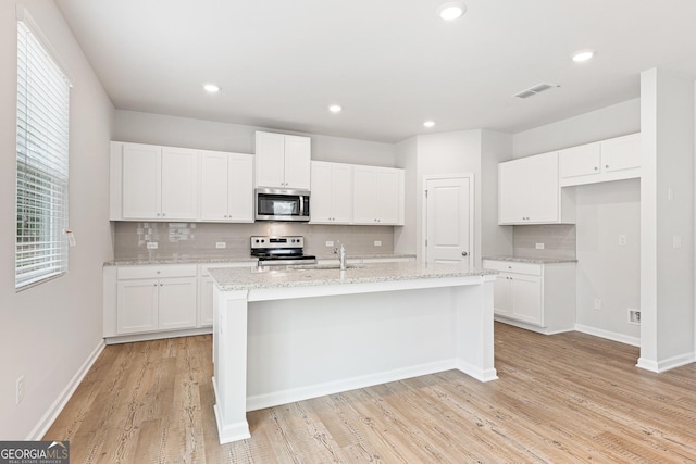 kitchen with white cabinetry, light stone counters, stainless steel appliances, and a center island with sink