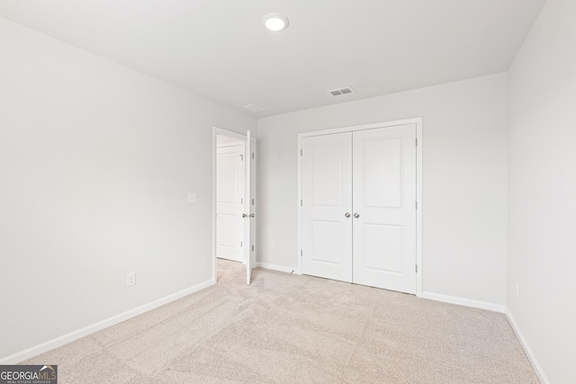 unfurnished bedroom with light colored carpet and a closet