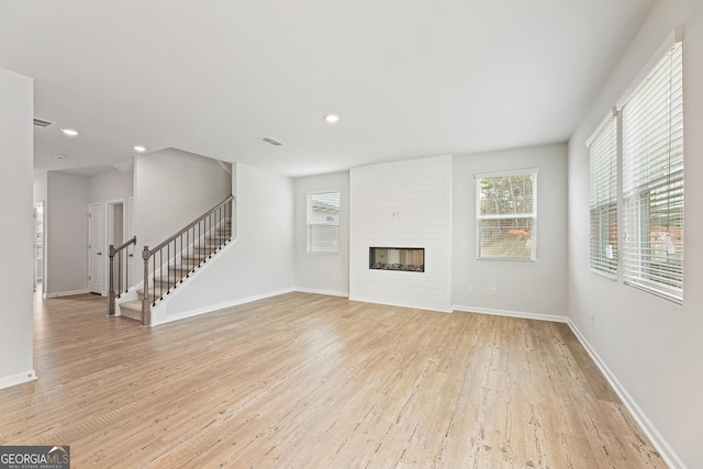 unfurnished living room with a large fireplace, a wealth of natural light, and light hardwood / wood-style floors