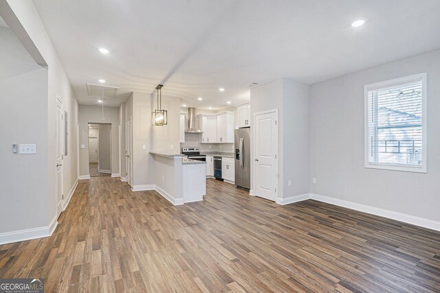 kitchen featuring dark wood-type flooring, appliances with stainless steel finishes, white cabinetry, hanging light fixtures, and wall chimney exhaust hood