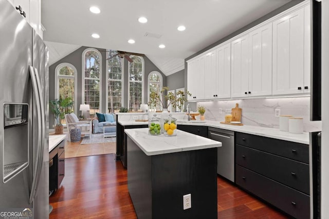 kitchen with appliances with stainless steel finishes, light stone counters, white cabinets, a kitchen island, and vaulted ceiling