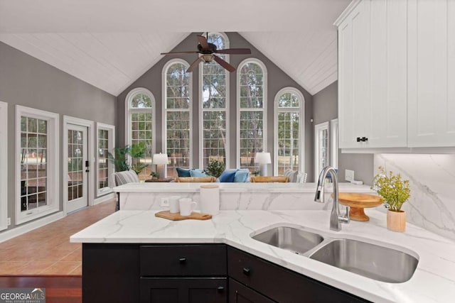 kitchen featuring high vaulted ceiling, white cabinetry, sink, ceiling fan, and light stone counters