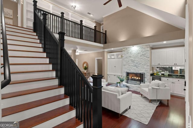 living room featuring ceiling fan, a towering ceiling, a fireplace, ornamental molding, and dark hardwood / wood-style flooring