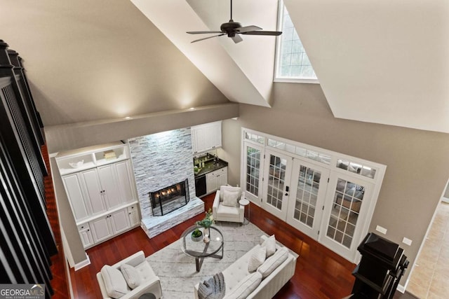 living room featuring dark wood-type flooring, ceiling fan, high vaulted ceiling, a stone fireplace, and french doors