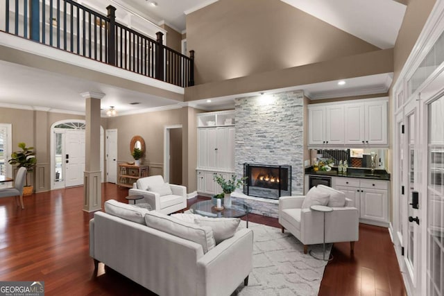 living room with crown molding, hardwood / wood-style floors, a stone fireplace, and ornate columns