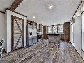 kitchen with wall chimney range hood, dark wood-type flooring, a center island, and appliances with stainless steel finishes