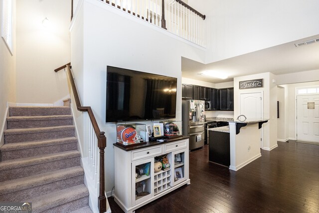 kitchen with dark wood-type flooring, a breakfast bar, appliances with stainless steel finishes, a kitchen island with sink, and a high ceiling