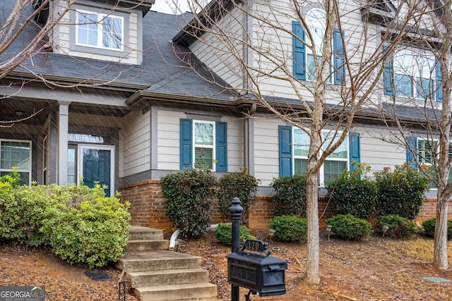 entrance to property featuring roof with shingles and brick siding