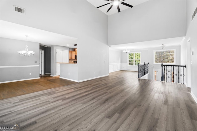 unfurnished living room featuring dark wood-type flooring, a towering ceiling, and ceiling fan with notable chandelier