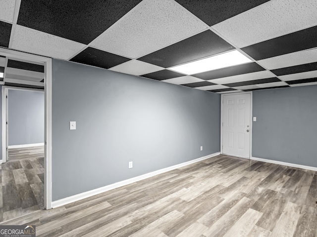 basement featuring a paneled ceiling and light hardwood / wood-style flooring