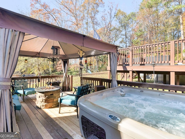 wooden deck featuring a gazebo, an outdoor fire pit, a hot tub, and a playground