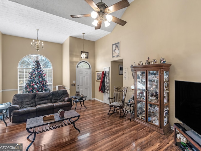 living room featuring dark hardwood / wood-style flooring, ceiling fan with notable chandelier, a textured ceiling, and a towering ceiling