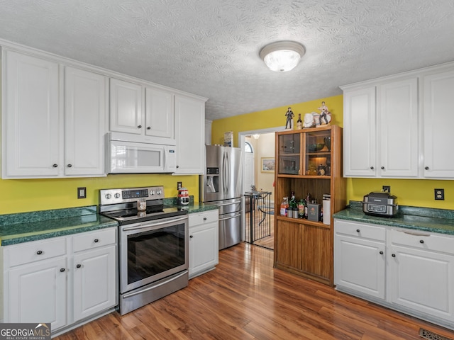 kitchen with stainless steel appliances, white cabinetry, dark wood-type flooring, and a textured ceiling