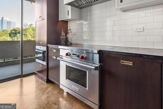 kitchen with backsplash, light parquet floors, dark brown cabinetry, stainless steel appliances, and custom range hood