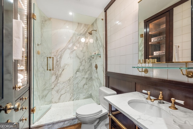 bathroom with a shower with door, vanity, tile walls, and toilet