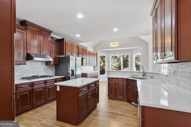 kitchen with sink, stainless steel appliances, a kitchen island, vaulted ceiling, and light wood-type flooring