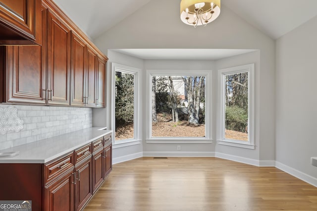 unfurnished dining area with vaulted ceiling, a healthy amount of sunlight, a chandelier, and light hardwood / wood-style flooring