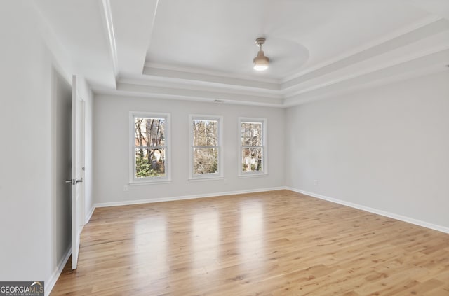 unfurnished room featuring a raised ceiling, crown molding, and light wood-type flooring