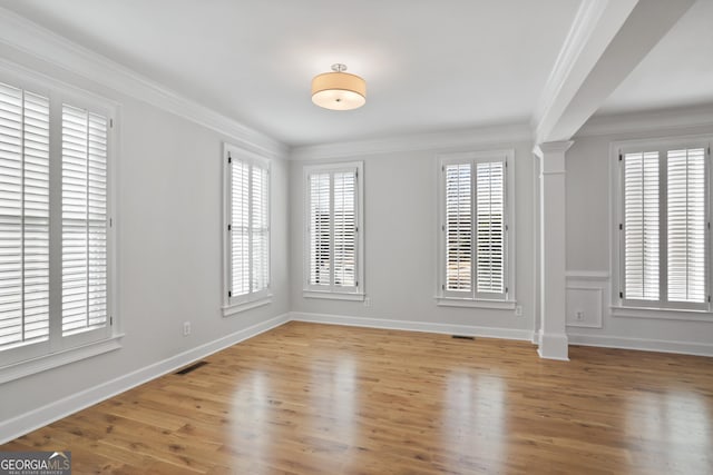 empty room featuring a healthy amount of sunlight, ornamental molding, and light wood-type flooring