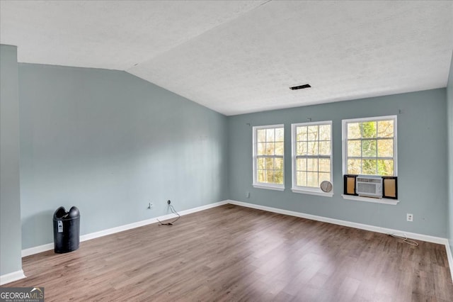 spare room featuring cooling unit, lofted ceiling, wood-type flooring, and a textured ceiling