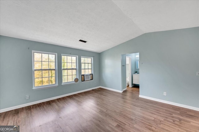 empty room featuring hardwood / wood-style flooring, vaulted ceiling, and a textured ceiling