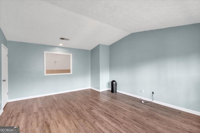 spare room with lofted ceiling, wood-type flooring, and a textured ceiling