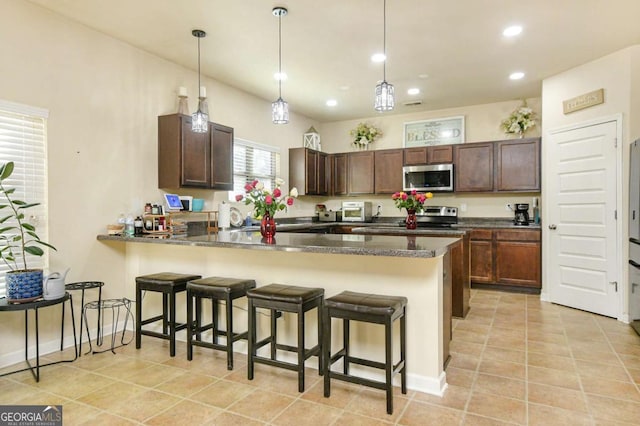 kitchen featuring light tile patterned floors, hanging light fixtures, stainless steel appliances, a kitchen bar, and kitchen peninsula