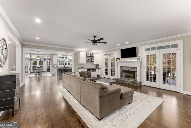 living room featuring hardwood / wood-style floors, crown molding, a stone fireplace, and french doors