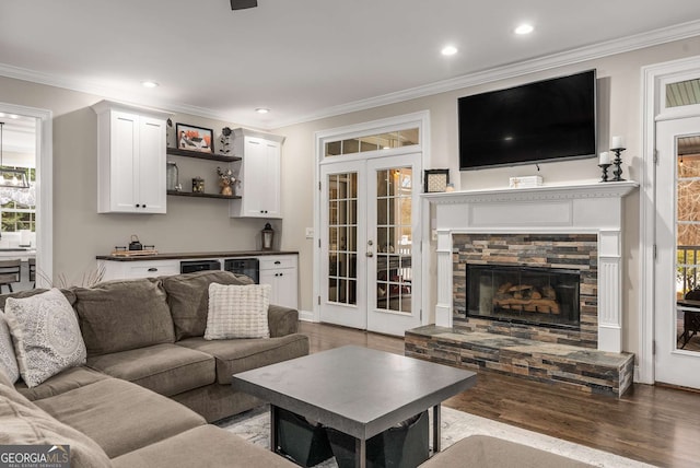 living room with ornamental molding, a stone fireplace, bar area, and wood-type flooring