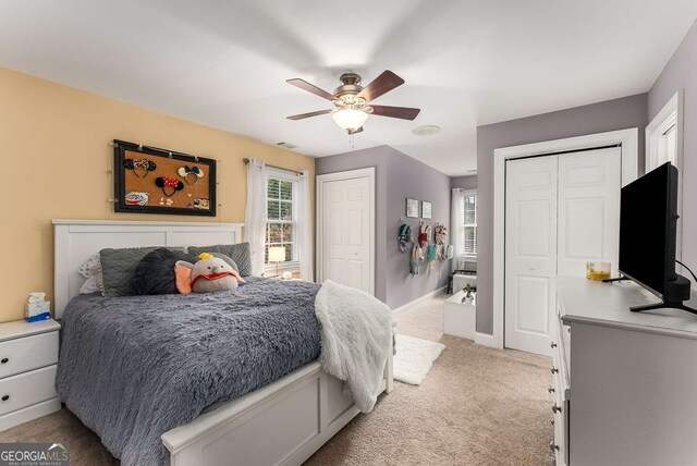 bedroom with two closets, light colored carpet, and ceiling fan