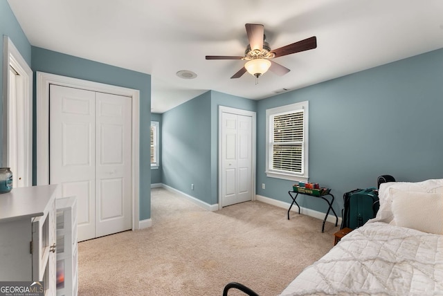 bedroom with multiple closets, light colored carpet, and ceiling fan