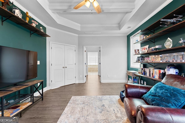 sitting room featuring a raised ceiling, wood-type flooring, ornamental molding, and ceiling fan