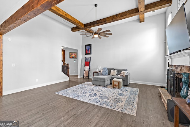 living room featuring beamed ceiling, ceiling fan, dark hardwood / wood-style floors, and a stone fireplace