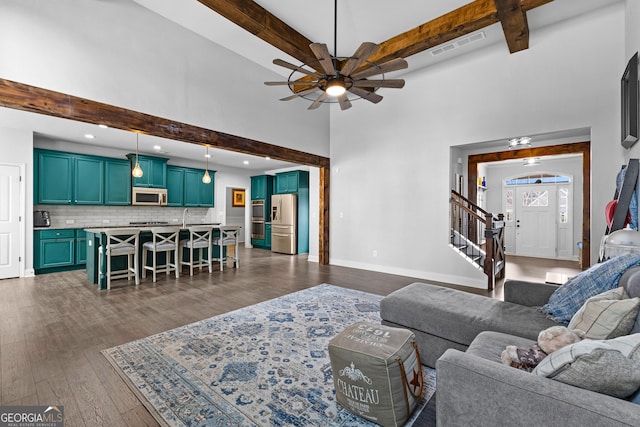 living room featuring beamed ceiling, ceiling fan, dark wood-type flooring, and a towering ceiling