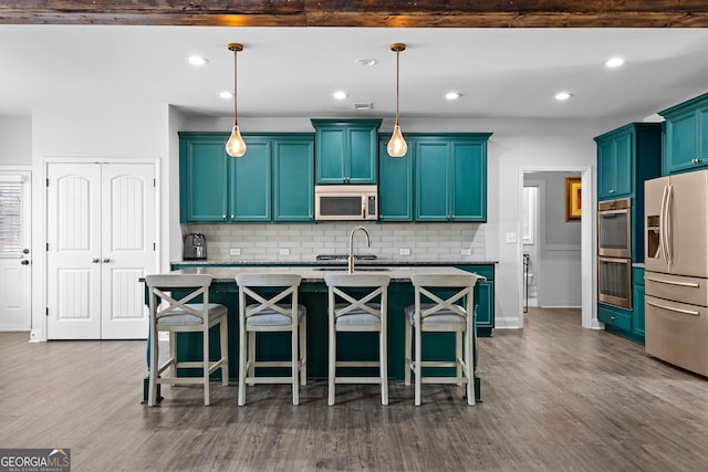 kitchen with pendant lighting, stainless steel appliances, a kitchen breakfast bar, and a center island with sink