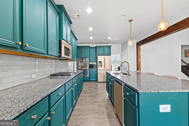 kitchen with sink, appliances with stainless steel finishes, pendant lighting, a kitchen island with sink, and decorative backsplash