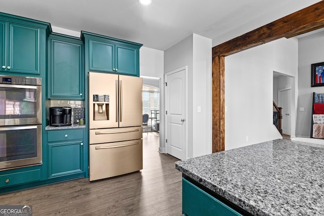 kitchen featuring dark wood-type flooring, blue cabinetry, stainless steel appliances, light stone counters, and tasteful backsplash