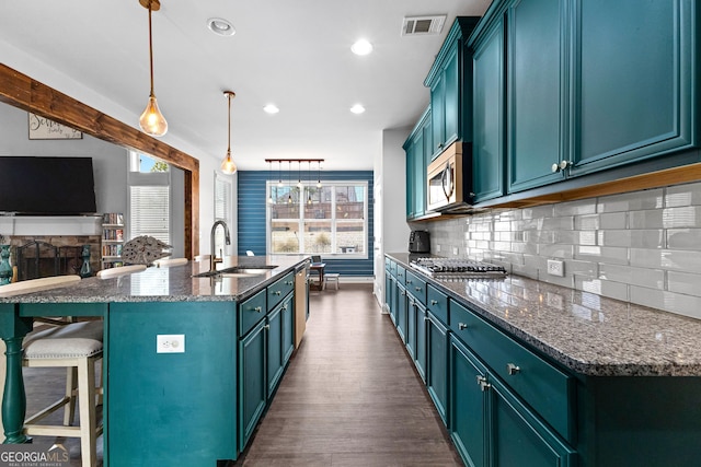 kitchen with decorative light fixtures, blue cabinets, an island with sink, sink, and stainless steel appliances