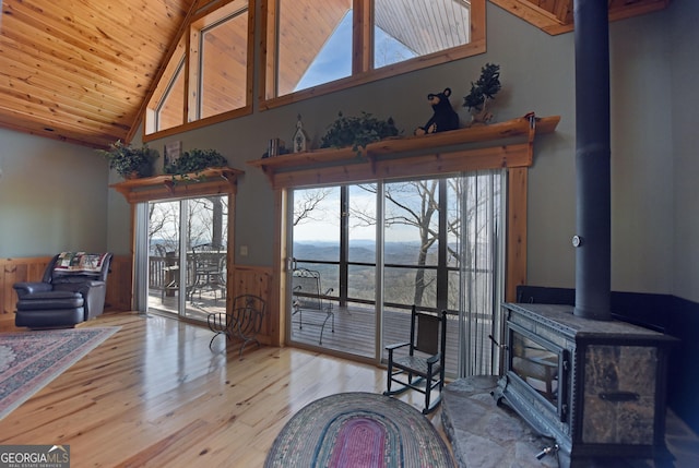 living room featuring high vaulted ceiling, wooden ceiling, light wood-type flooring, and a wood stove