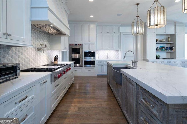 kitchen featuring premium range hood, white cabinetry, an island with sink, pendant lighting, and stainless steel appliances