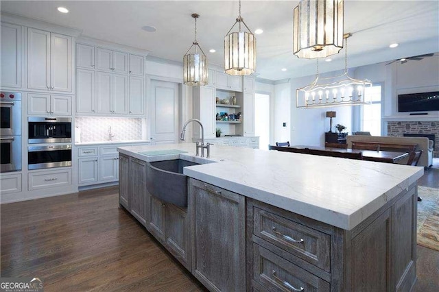 kitchen with white cabinetry, sink, hanging light fixtures, light stone counters, and a center island with sink