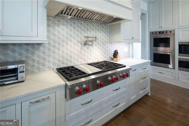 kitchen featuring appliances with stainless steel finishes, dark hardwood / wood-style floors, white cabinetry, custom exhaust hood, and light stone countertops