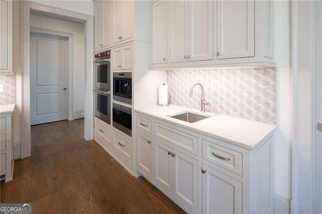 kitchen featuring double oven, tasteful backsplash, white cabinetry, sink, and dark wood-type flooring