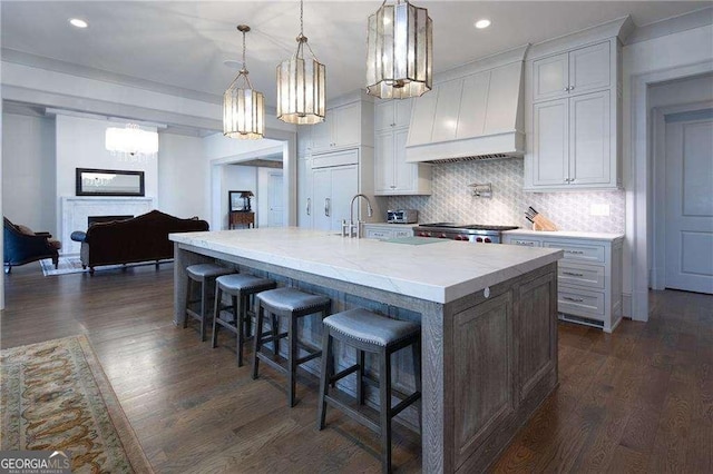 kitchen featuring pendant lighting, a breakfast bar area, backsplash, custom range hood, and a center island with sink