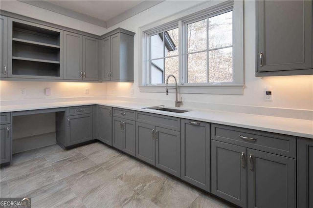 kitchen with gray cabinetry, sink, and built in desk